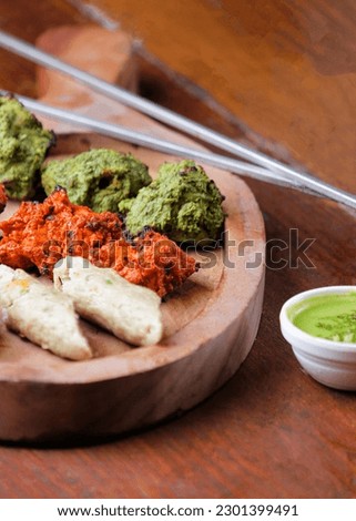 Non veg barbeque mixed grill platter 3 color orange green white serve on wooden tray with side dip chutney Indian restaurant food menu dish close view photography