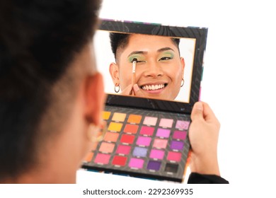 non-binary asian person applying eyeshadow with colorful makeup case looking in the mirror on white background - Powered by Shutterstock