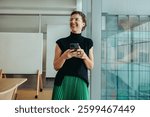 A non-binary entrepreneur smiling confidently while using her smartphone. She stands in a modern office environment, conveying themes of success, innovation, and professional achievement.