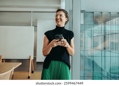 A non-binary entrepreneur smiling confidently while using her smartphone. She stands in a modern office environment, conveying themes of success, innovation, and professional achievement.