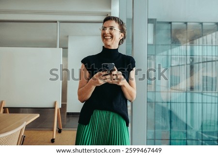 A non-binary entrepreneur smiling confidently while using her smartphone. She stands in a modern office environment, conveying themes of success, innovation, and professional achievement.