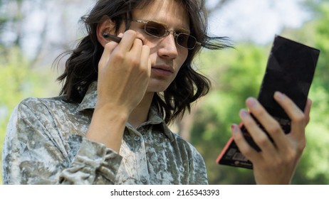 Non-binary Gender Person Applying Makeup In A Park, Using A Brush.