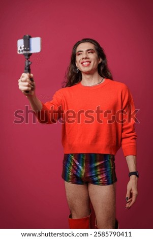 Non-binary person creating content with their cell phone on a red background, studio photo, with copy space