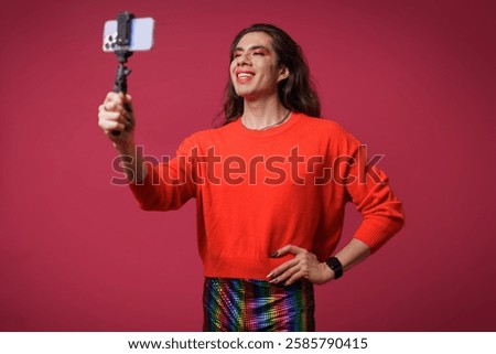 Non-binary person creating content with their cell phone on a red background, studio photo, with copy space