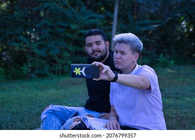 Non-binary Person And Gay Guy, Sitting On Grass, Taking Selfie With Cell Phone. Concept Non-binary, Gay, Lgbtq+, Inclusion, Lesbian, Lgbtq.