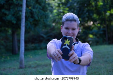 Non-binary Person, Sitting On The Lawn, With Gay Pride Flag And Taking A Selfie With Cell Phone. Non-binary Concept, Lgbtq+, Inclusion, Gay, Lesbian, Lgbtq.