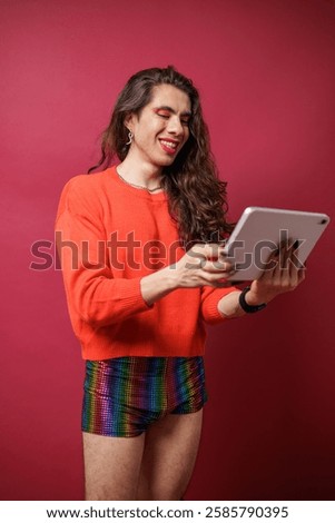 Non-binary person using a tablet on a red background and wearing pride clothing