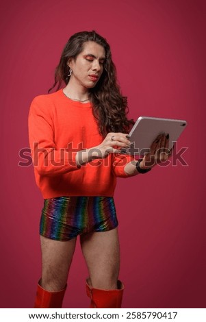 Non-binary person using a tablet on a red background and wearing pride clothing