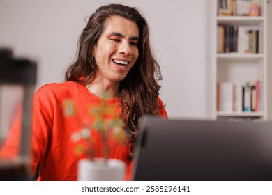 Non-binary person working from home on their laptop with a big smile