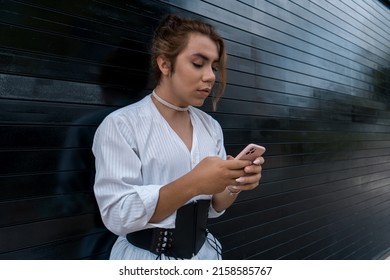 non-binary using phone in her hands chating leaning on black gate in the street remembering - Powered by Shutterstock