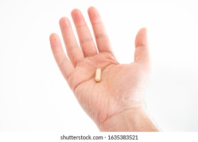 Nondescript medical pill held in palm by Caucasian male hands close up shot isolated on white 2020
