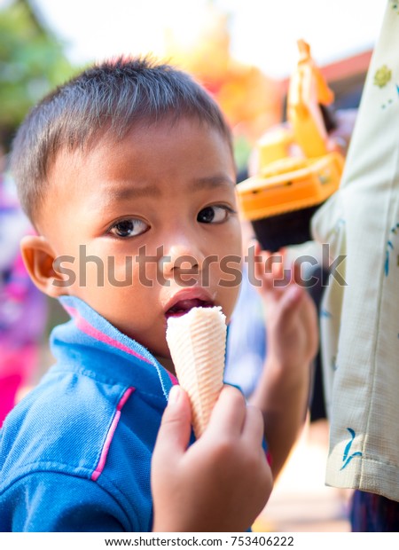 Nong Bua,Thailand - October 31, 2017 : Little child\
boy eat delicious ice cream and looking on camera. A cute asian shy\
boy enjoy eating with white ice cream and playing a yellow toy car\
with mom.