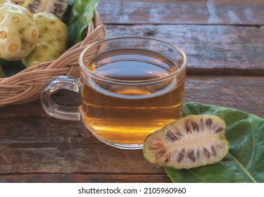 Noni herbal juice drink in glass cup with fresh noni in basket and on old wooden background.