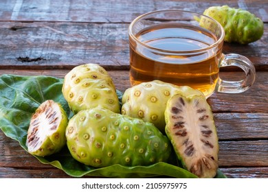 Noni Herbal Juice Drink In Glass Cup With Fresh Noni In Basket And On Old Wooden Background.