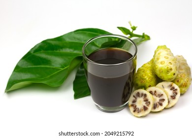 Noni juice in glass and noni fruit with green leaf isolated on white background.