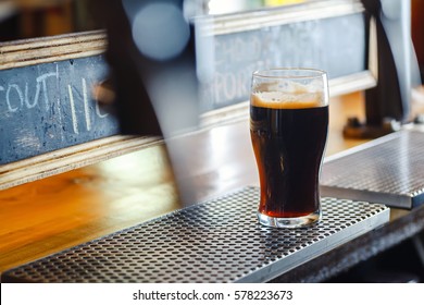 Nonic Pint Glass With Dark Stout Ale Standing On A Pub Counter Near Draft Taps