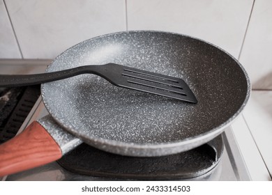 Una sartén antiadherente de teflón con una espátula de plástico en la estufa, utensilios de cocina, en la cocina.