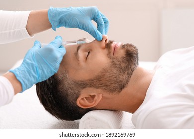 Nonsurgical rhinoplasty concept. Middle-aged bearded businessman visiting aesthetic clinic, getting injection in his nose, side view. Nose filler for handsome man at beauty salon