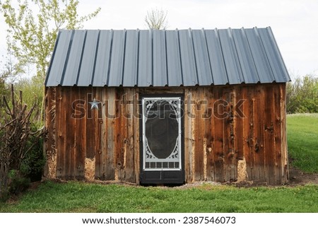 Non-urban scene of a small rustic wooden shed with a grey tin roof and fresh green grass.