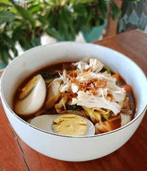 Noodle Soup Mixed With Chicken, Eggs, Vegetables And Meatballs In A White Bowl On A Closeup Wooden Table Ready To Eat