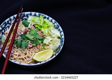 Noodles Served In Bowls With Lemon Wedges, Coriander Garnish And Minced Pork Are Placed On A Black Table.