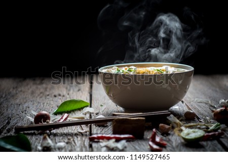 Noodles with steam and smoke in bowl on wooden background, selective focus. Asian meal on a table, junk food concept