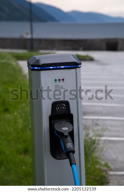 Nordfjordeid, Norway - June 26, 2022: A static\
shot of a solid black Tesla Model 3 dual motor charging at the\
Nordfjordeid municipality AC charging station in a cloudy spring\
day. Selective\
focus.