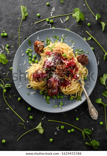 Nordic style comfort\
food. Linguine pasta in nests and homemade meatballs with green\
peas, lingonberry sauce, cilantro and cheese on grey plate on black\
background top view 