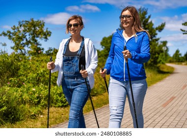 Nordic walking - two mid-adult beautiful women exercising in city park using Nordic walking poles  - Powered by Shutterstock