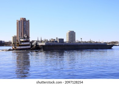 Norfolk, VA, USA - December 26, 2021: A Tugboat Pushing A Barge Along The Elizabeth River With The Skyline Of The City Of Portsmouth In The Background.