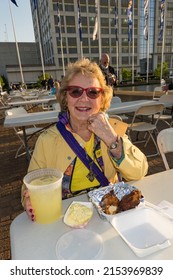 Norfolk, Virginia,  April 29, 2022 A Woman In A Yellow Jacket Is Eating And Drinking Outside With Lemonade At The Norfolk Scope Arena.