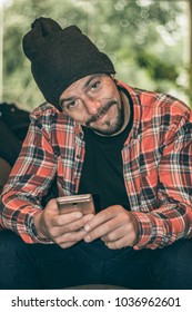 Normal Guy Staring At His Cell Phone In A Coffee Shop. Casual Dress With Hat On The Head