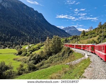 A normal passenger red train driving through the countryside in Switzerland, Europe. Traveling by train in Switzerland is very popular among locals and tourists alike. The trains run on time.