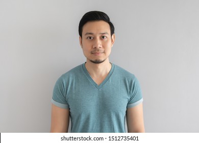 Normal straight face portrait of Asian man in blue t-shirt on grey background.