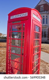 NORMAN, OKLAHOMA - DECEMBER 16, 2013: A Bright Red, British Style Telephone Booth Stands Ready On An American University Campus Under A Blue Sky.