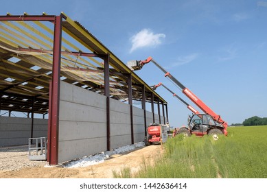 Normandy, France, March 2008.
Construction Of A New Farm Building For Cows Breeding With A Steel Frame. Roof Sheathing Installation. Roofer On The Roof. Installation Of Safety Net As Fall Prevention