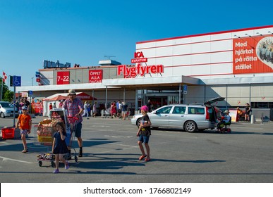 Norrtalje, Sweden - June 25 2020:
The Front Of A Store Called Ica Flygfyren In Norrtalje City.
A Dad And His Kids Are Done Shopping And Walks Towards Their Car With Their Grocery Cart. 