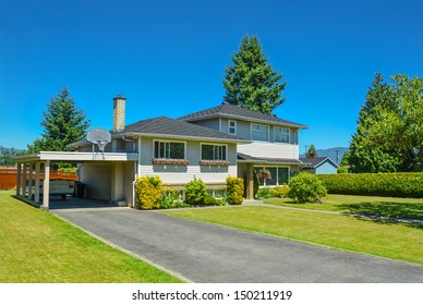 North American Family House With Big Front Yard And Blue Sky Background. Family House With Asphalt Driveway And Parking Under Roof.