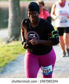 North Babylon, New York, USA – 8 July 2019: Runner smiling while racing a 5K at Belmont Lake State Park on a path around the lake with a blurred background.