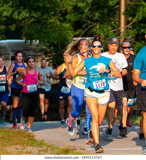 North Babylon, New York, USA
- 8 July 2019: A femlae runner is waving and smiling for the camera
while running a 5K as she enters bright sunshine in a crowded
race.