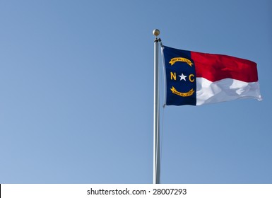 A North Carolina State Flag waving in the wind against a clear blue sky.