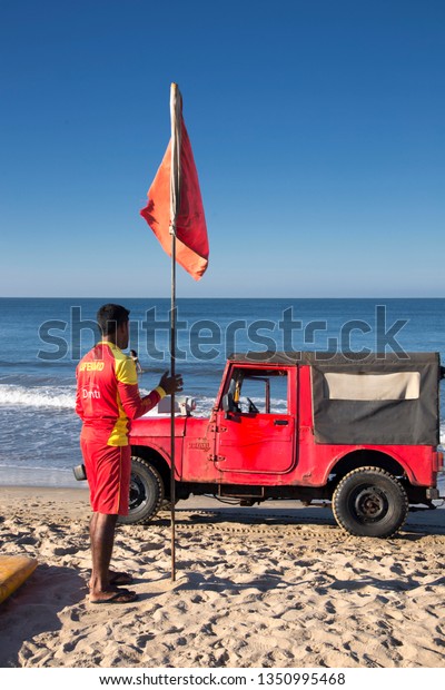 North\
Goa, Arambol, Mandrem / India - December 2018:Men rescuers walk\
along the shore in red clothes, whistle in the whistle, warn of\
danger in the sea and expel people from the\
sea