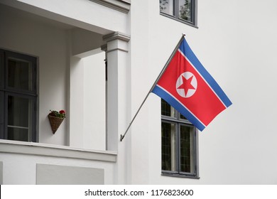 North Korea Flag. North Korean Flag Hanging On A Pole In Front Of The House. National Flag Waving On A Home Displaying On A Pole On A Front Door Of A Building. Flag Raised At A Full Staff.