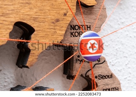 North Korea flag on the pushpin with red thread showed the paths of movement or areas of influence in the global economy on the wooden map. Planning of traveling or logistic concept. Network