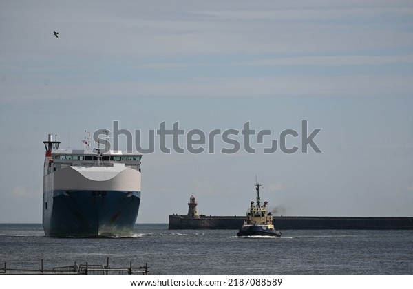 North Shields, England - August 6 2022: Nordic\
Ace car transport vessel entering mouth of River Tyne supported by\
pilot tug vessels