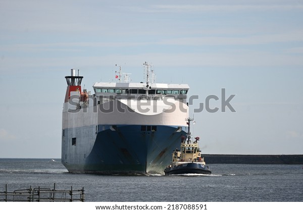 North Shields, England - August 6 2022: Nordic\
Ace car transport vessel entering mouth of River Tyne supported by\
pilot tug vessels