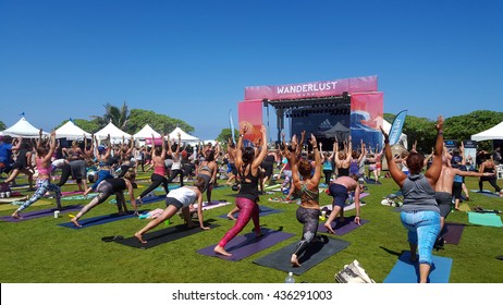 NORTH SHORE, HAWAII - FEBRUARY 28: People raise arms over head in warrior one during outdoor yoga class facing stage at Wanderlust yoga event on the North Shore, Hawaii on February 28, 2016.