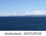 The northbound ferry to Oslo is near Kullen peninsula belonging to Sweden. It and the Kullaberg on it are visible on the horizon. The Sea Öresund is calm and there are only some clouds visible.