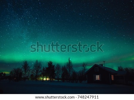 Northern lights (Aurora Borealis) over snowed-in cottage in Lapland village. Finland