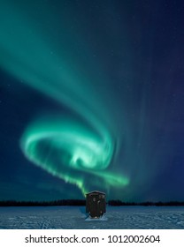 Northern Lights Glowing Over An Ice Fishing Hut.